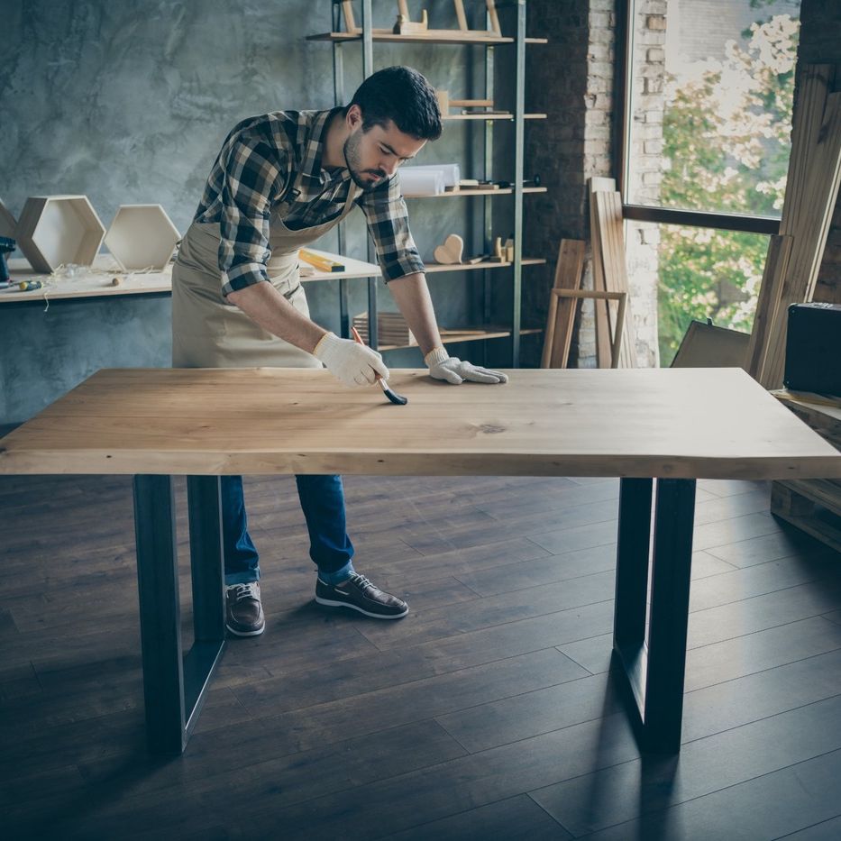 carpintero joven barnizando una tabla sujetada sobre atril